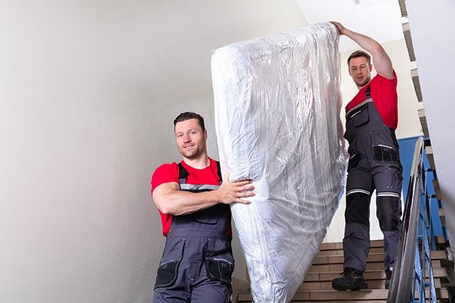 two workers carrying a heavy box spring out of a bedroom in Newport